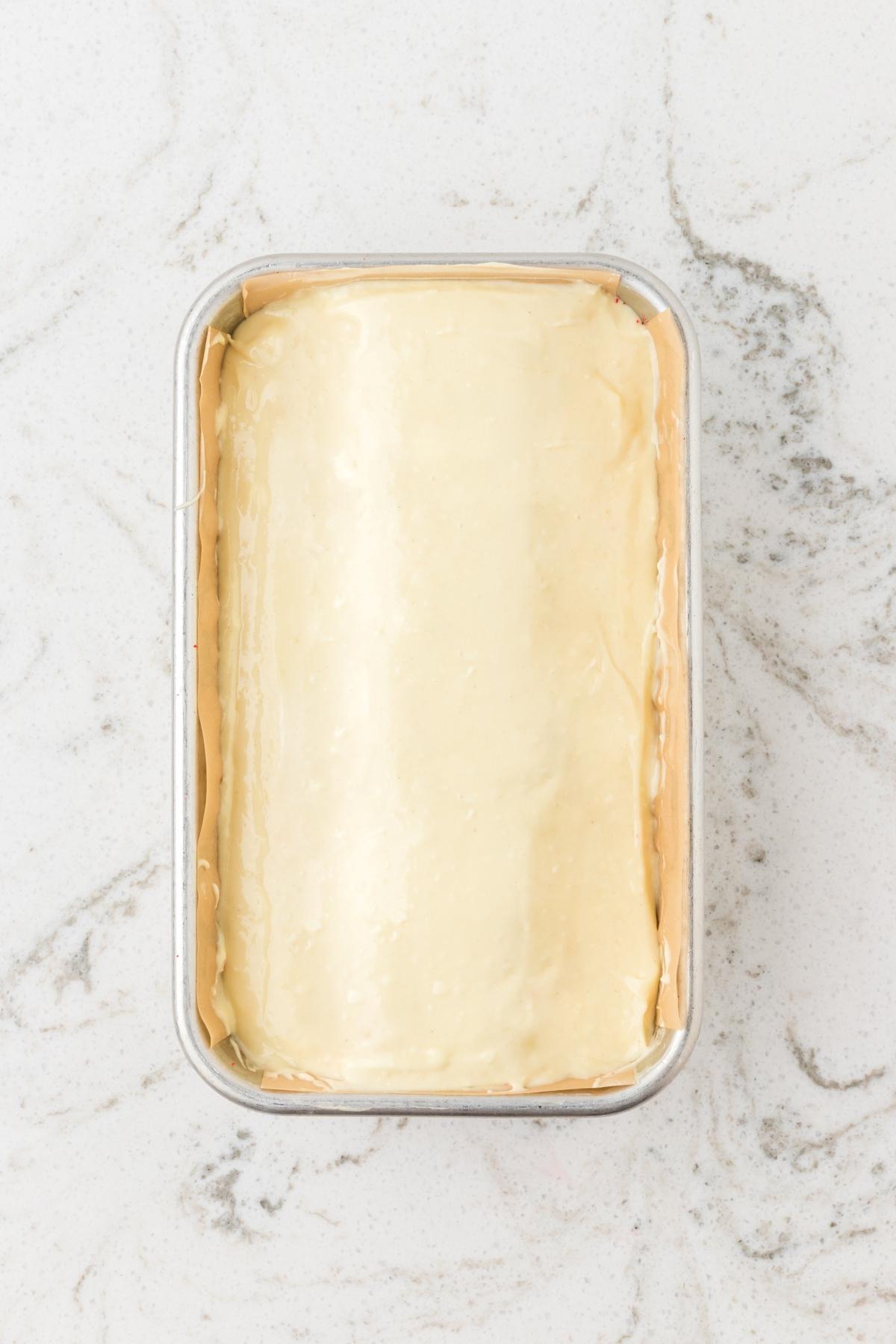 A loaf pan filled with unbaked pastry dough on a light marble surface.