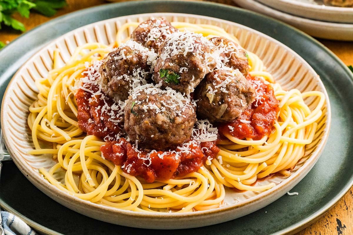 A plate of spaghetti topped with tomato sauce, best Italian meatballs, and grated cheese.