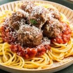 A plate of spaghetti topped with tomato sauce, best Italian meatballs, and grated cheese.