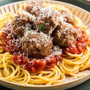 A plate of spaghetti topped with tomato sauce, best Italian meatballs, and grated cheese.