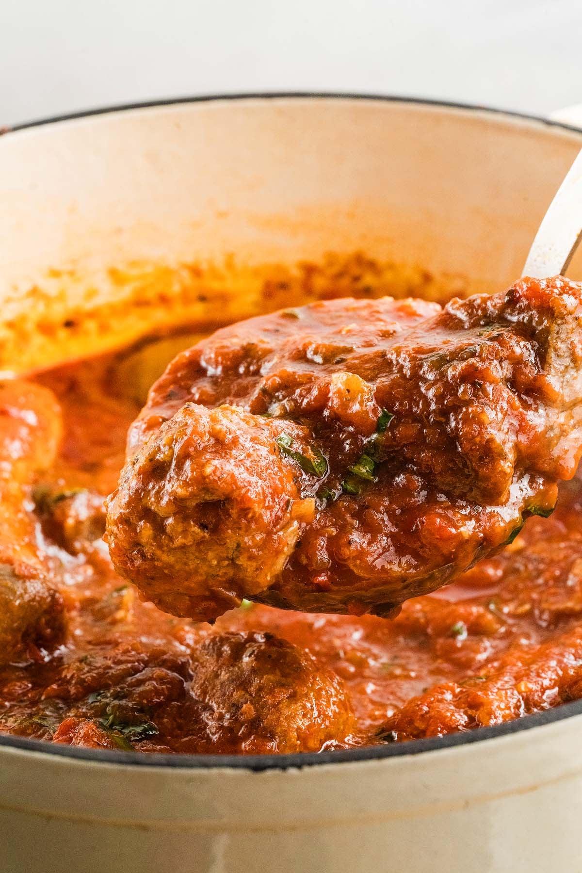 A ladle scoops meatballs in rich Sunday Sauce from a large pot.