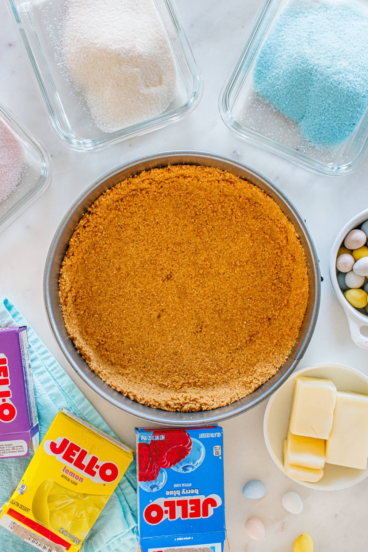 Round graham cracker crust in a pan, with Jello boxes, butter, and sugar in containers around it.