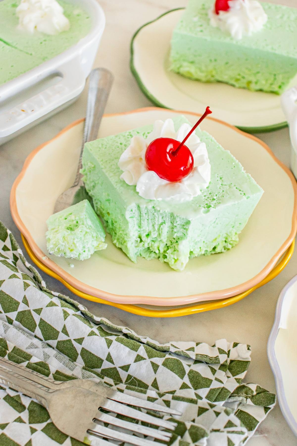 A slice of lime Jello salad dessert topped with whipped cream and a cherry, with a forkful taken out.