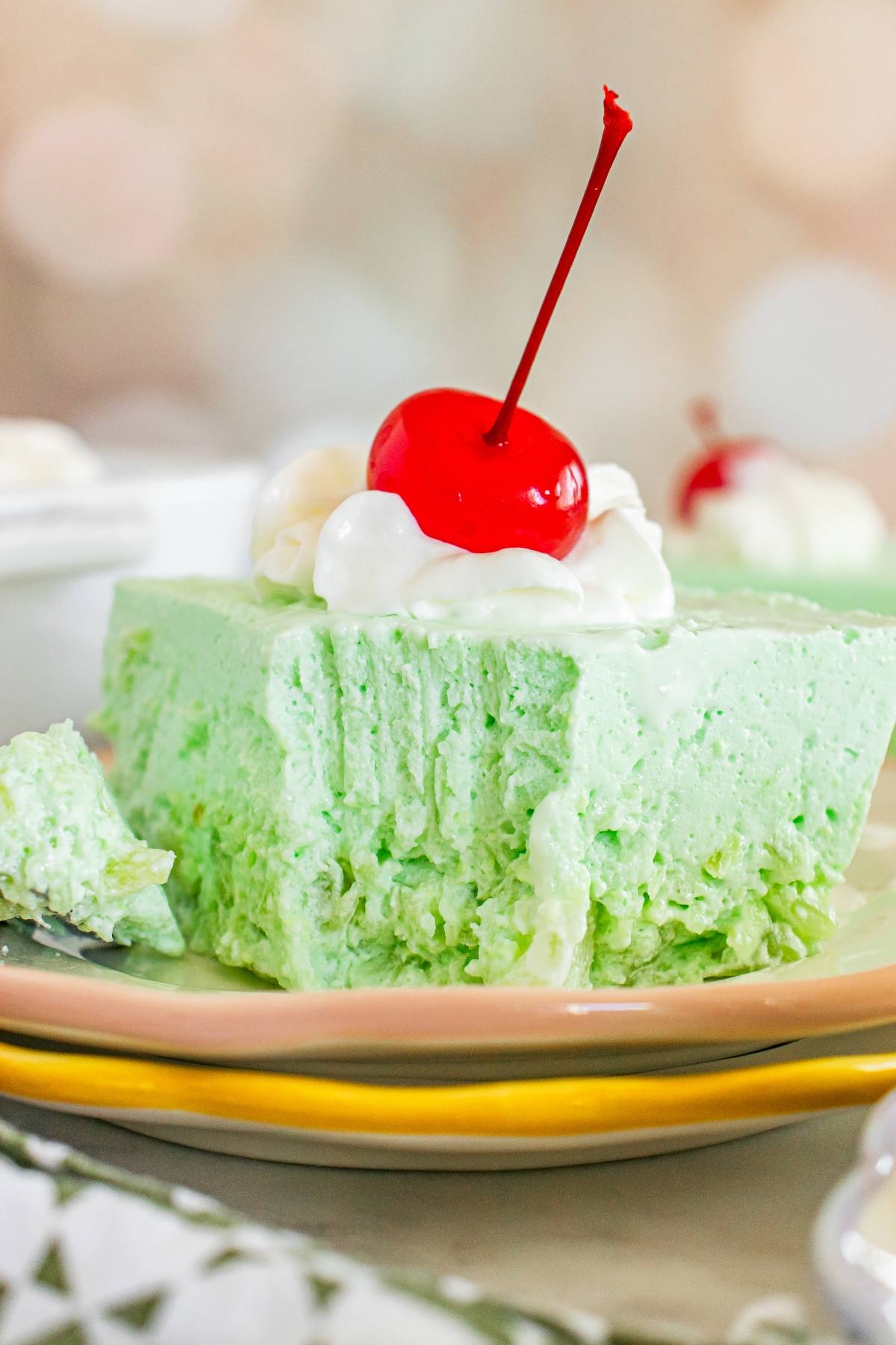 A slice of lime Jello salad dessert with whipped cream and a cherry on top, served on a plate.