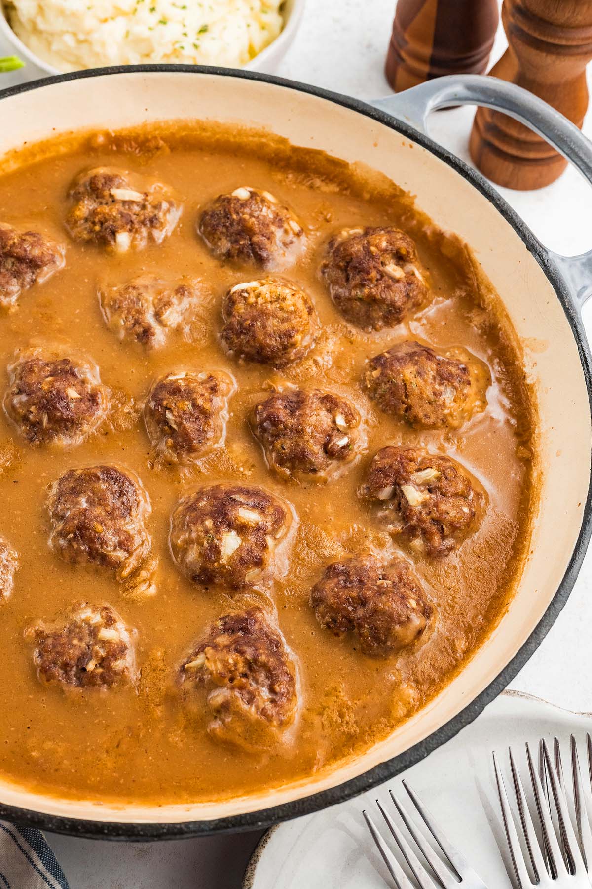Meatballs and gravy simmer in brown sauce in a large skillet, with plates and forks nearby.