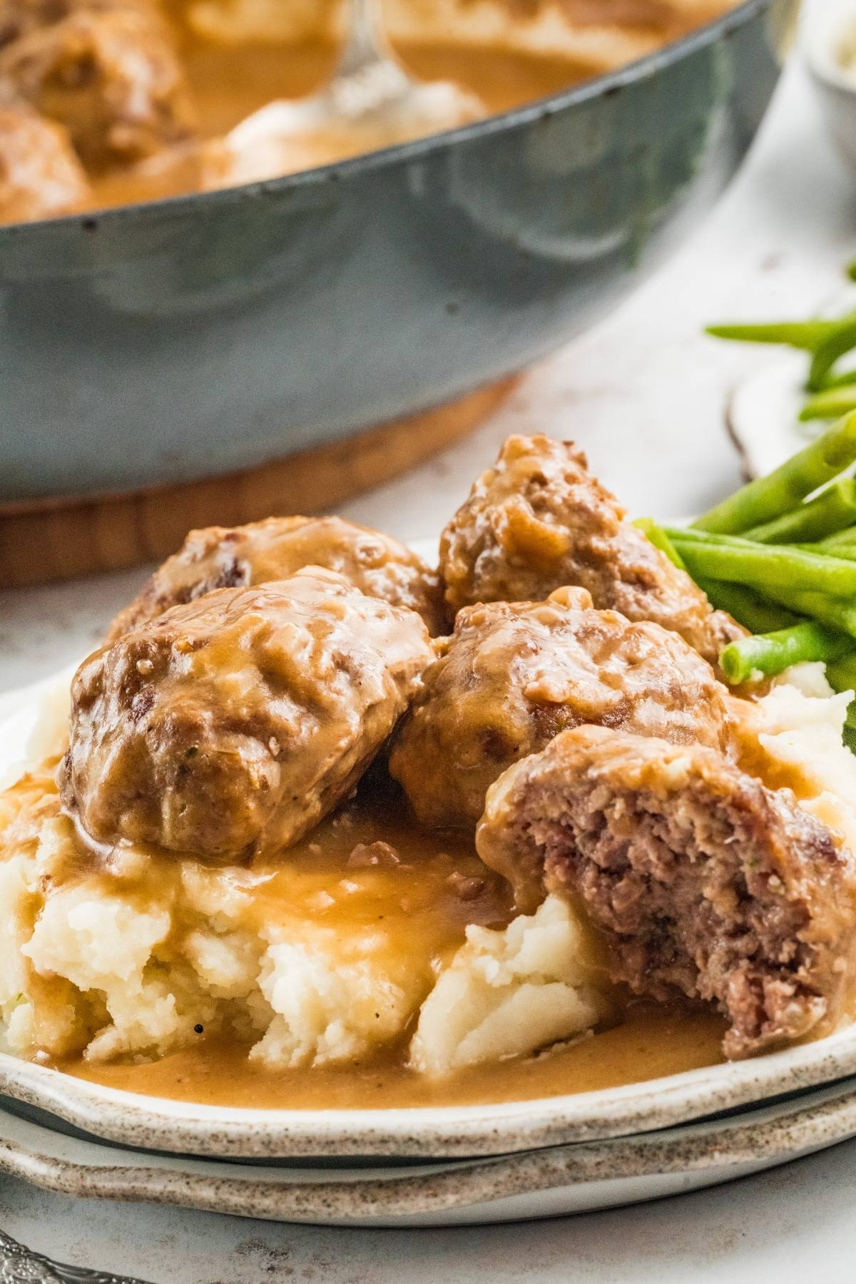Meatballs with brown gravy on mashed potatoes, served with green beans on a plate.
