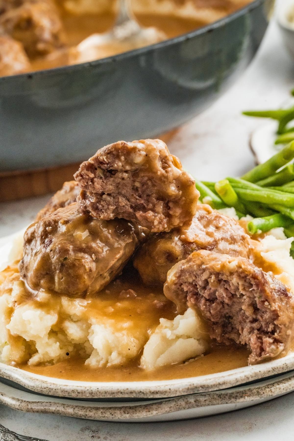 Mashed potatoes topped with Salisbury steak and brown gravy, with green beans on the side.
