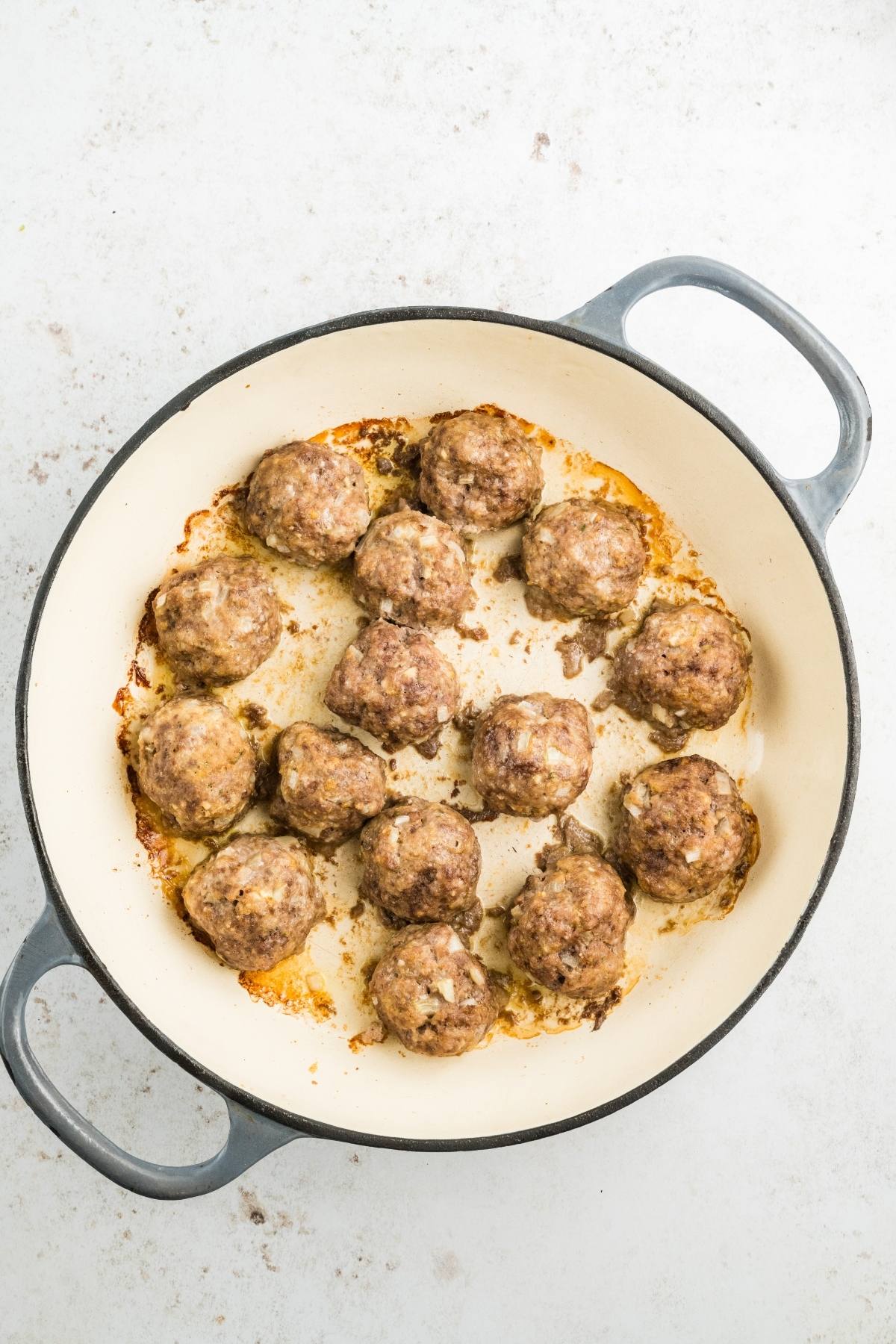 A round, white baking dish with cooked meatballs arranged inside, viewed from above on a light background.