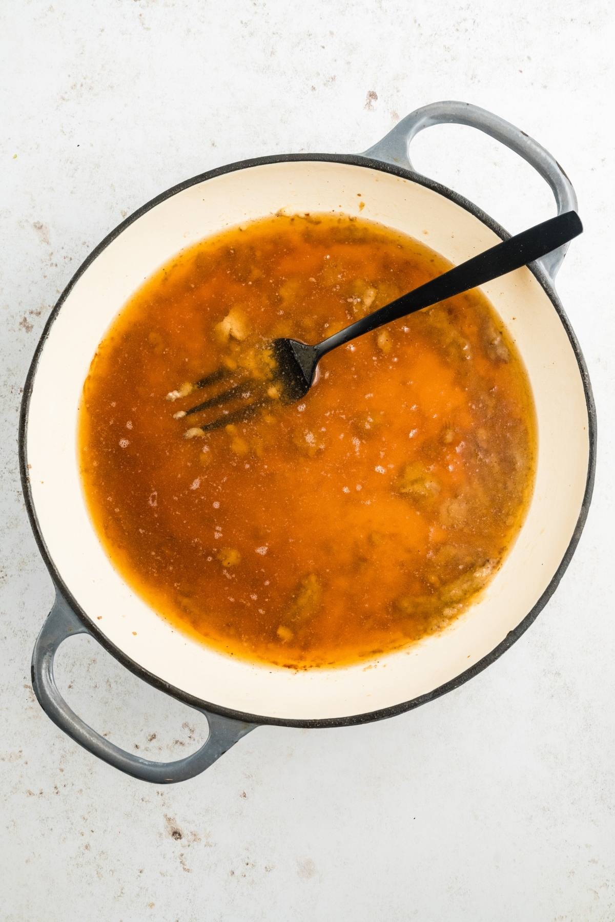 A pot with orange-brown liquid and a black spatula on a white surface.