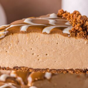 A close-up of a creamy no bake Biscoff cheesecake slice with a crumbly crust and decorative caramel topping.