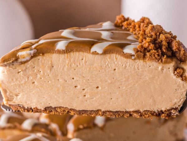 A close-up of a creamy no bake Biscoff cheesecake slice with a crumbly crust and decorative caramel topping.