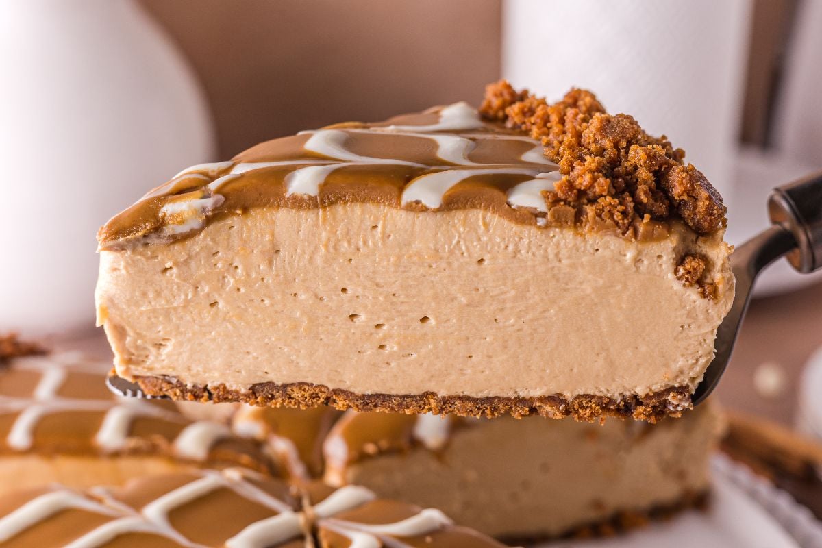 A slice of creamy no bake Biscoff cheesecake with a cookie crust and decorative white icing on top.