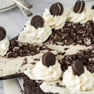 No Bake Oreo Cheesecake topped with whipped cream swirls and mini chocolate sandwich cookies on a plate.
