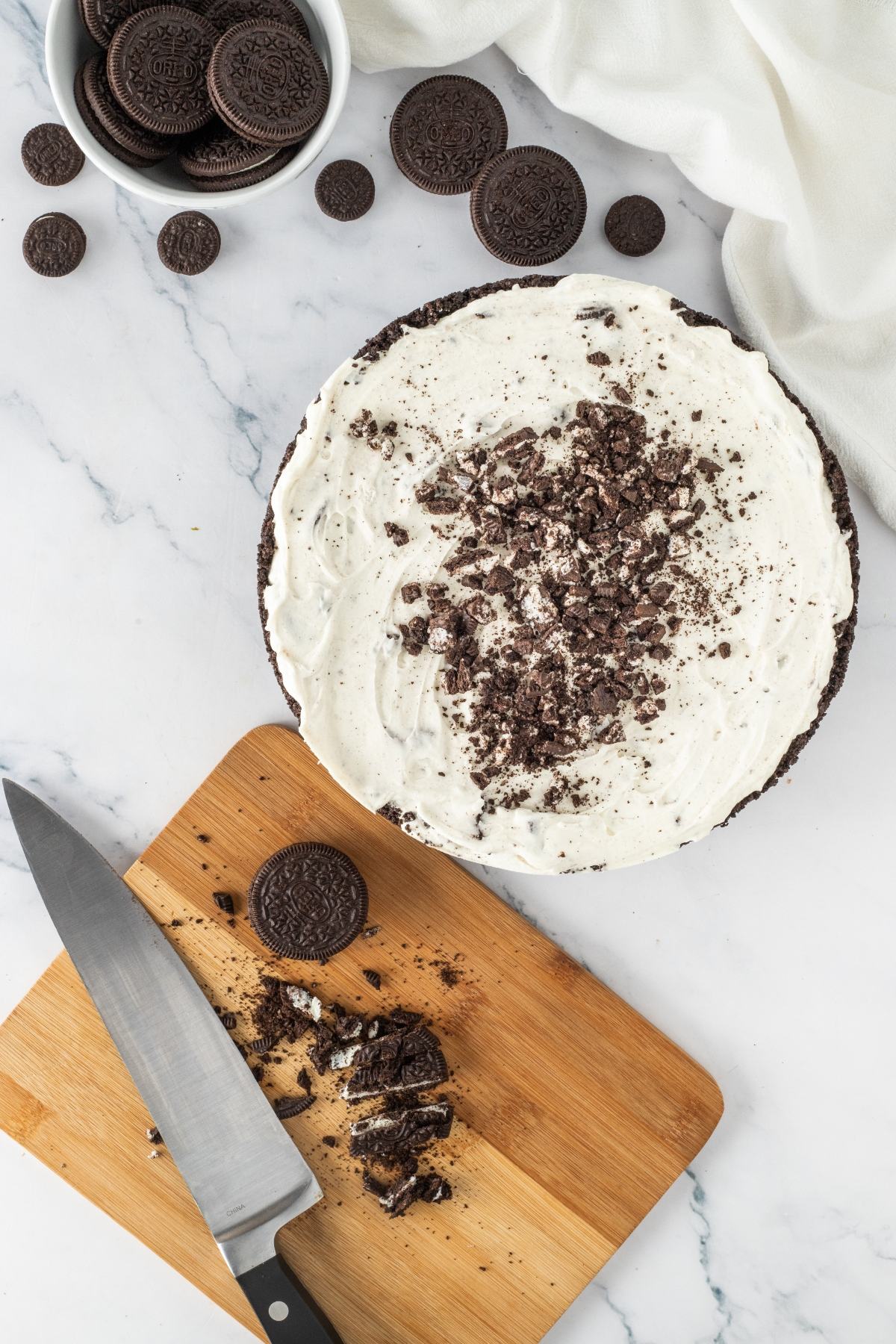 Oreo cream pie with crumbled cookies on top, a knife, and whole cookies on a cutting board and in a bowl.