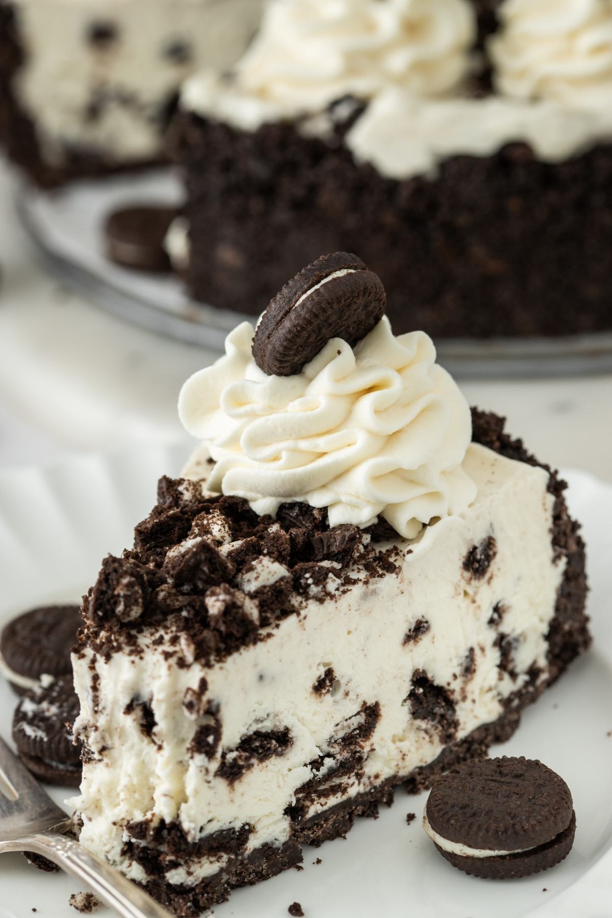 A slice of cookies and cream cheesecake topped with whipped cream and a mini chocolate cookie.