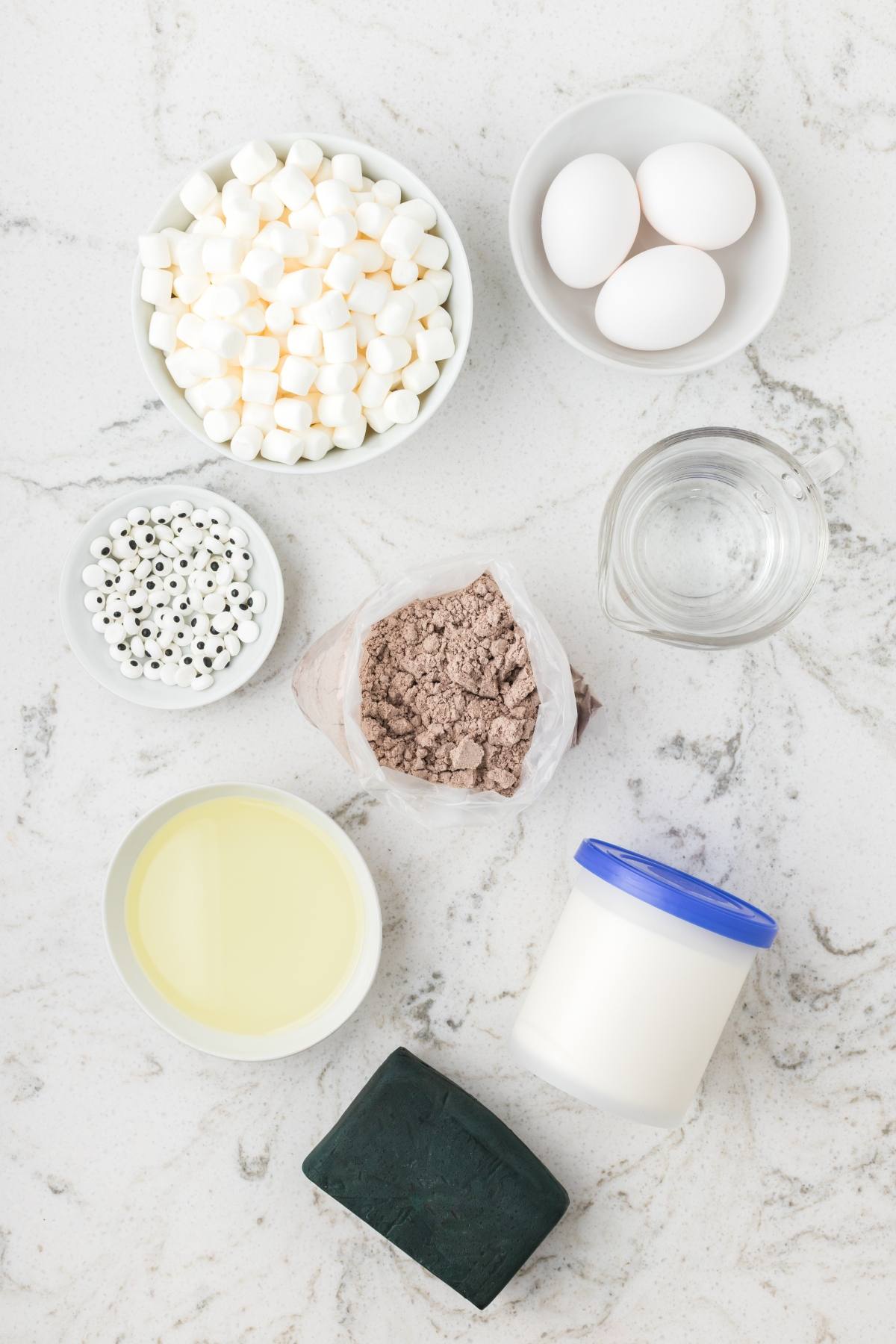 Baking ingredients on a countertop: eggs, water, oil, marshmallows, yogurt, cake mix, and candy eyes.