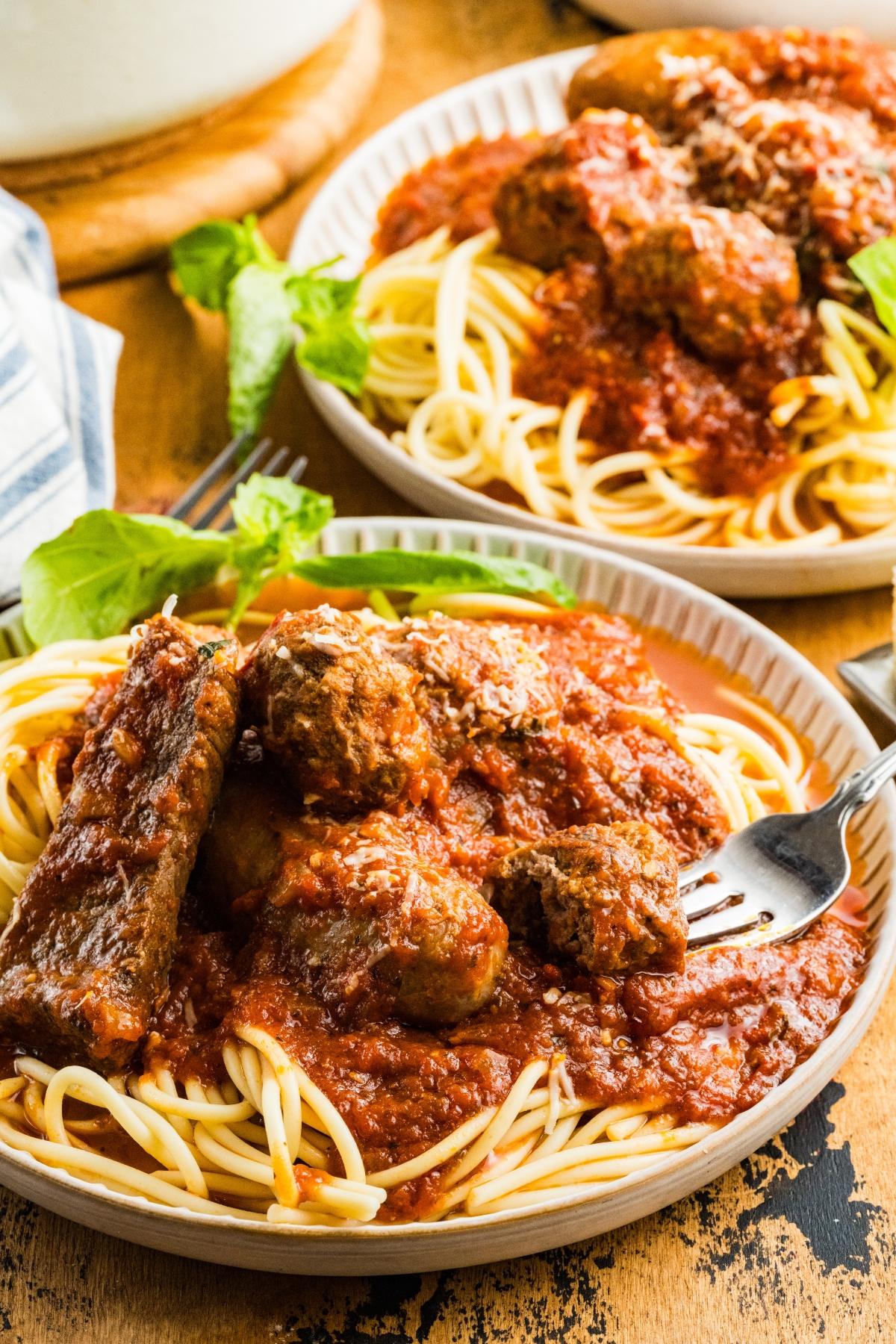 Plates of spaghetti topped with tomato sauce and meatballs, garnished with fresh basil leaves.
