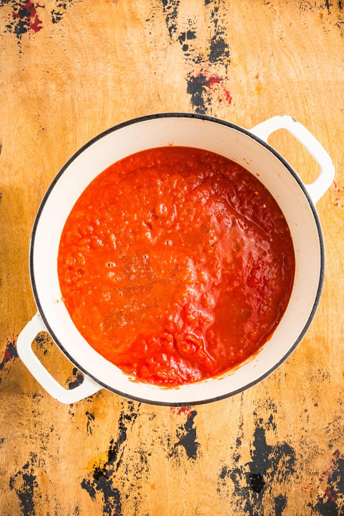 A white pot filled with red tomato sauce sits on a rustic wooden surface.
