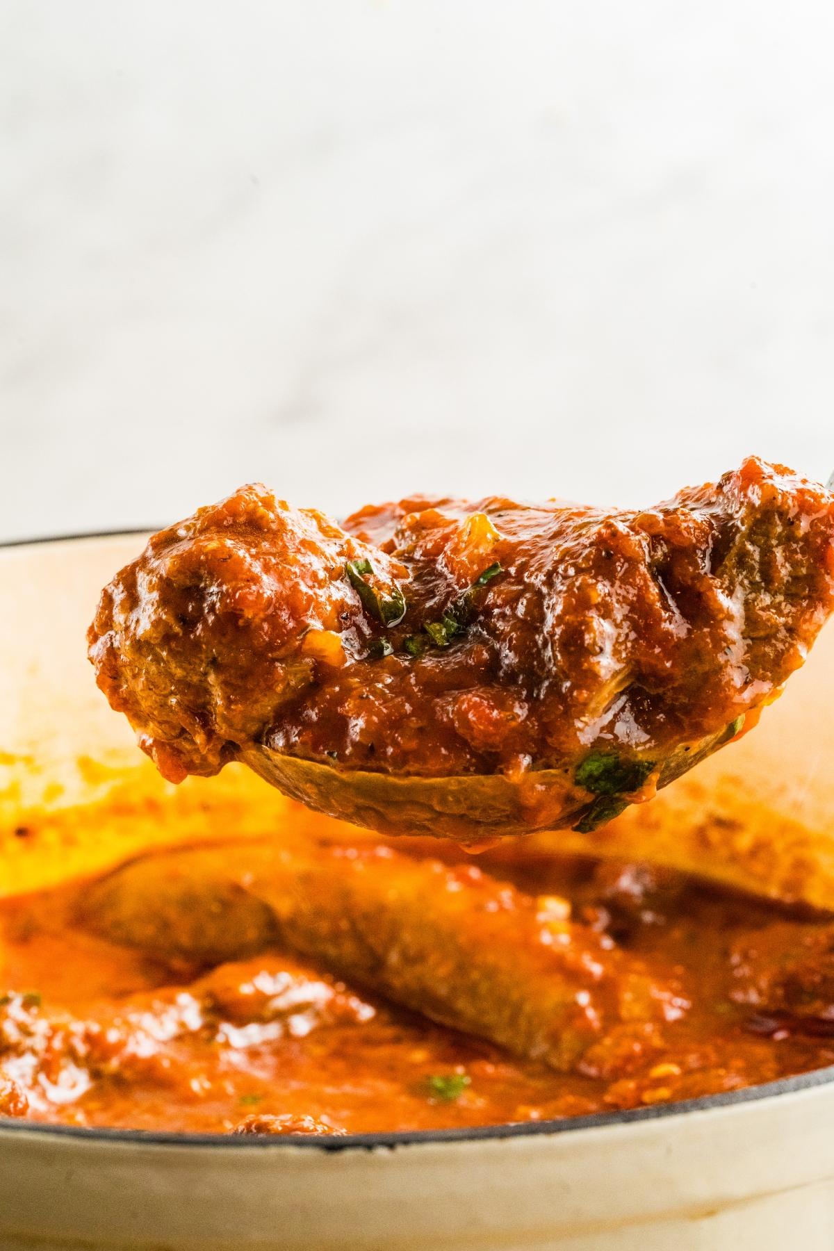 A spoon lifts meatballs covered in tomato sauce from a pot.