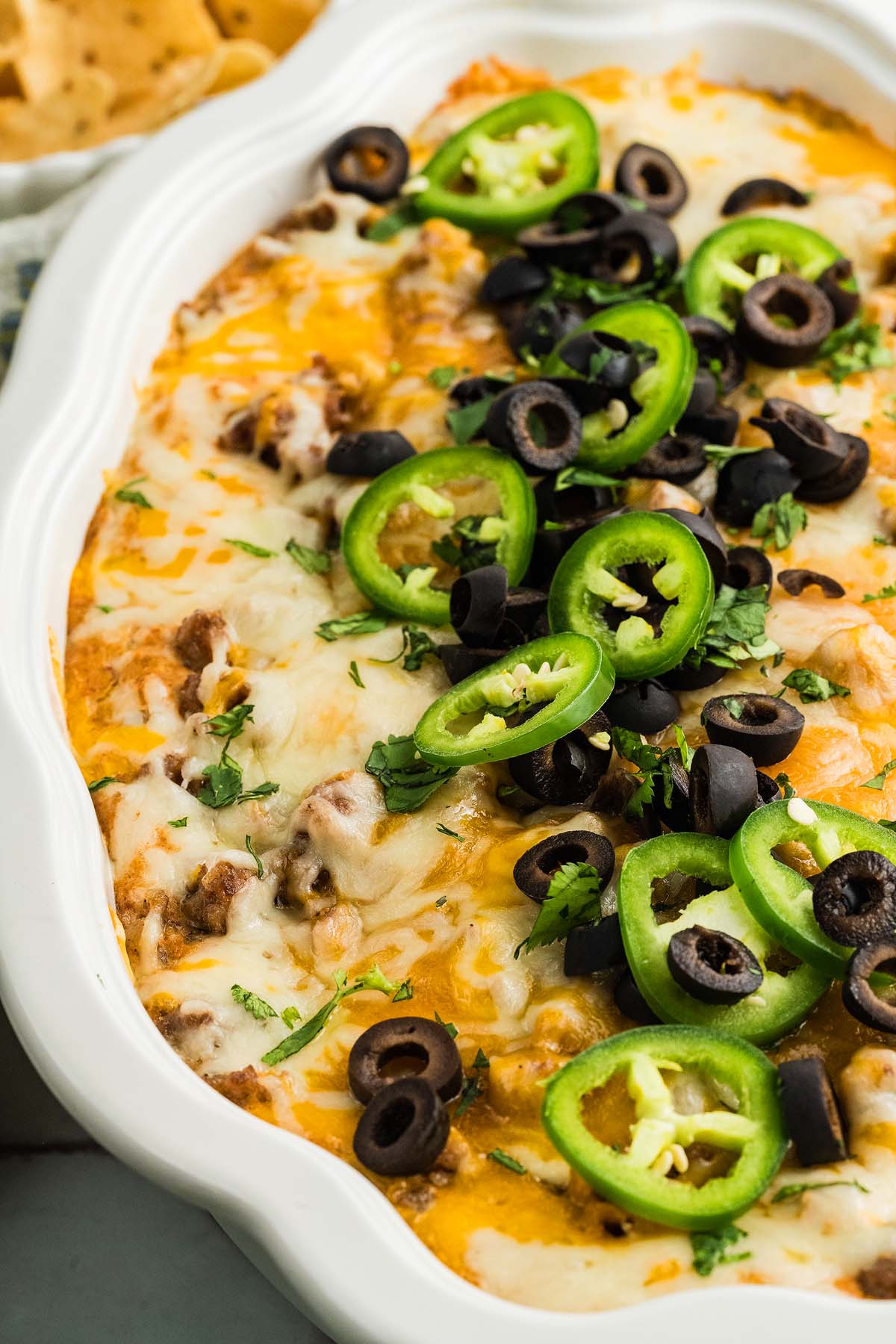 Cheesy Texas Trash Dip baked to perfection, topped with sliced jalapeños, black olives, and chopped cilantro in a white dish.