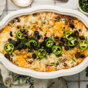 Texas Trash Dip baked casserole topped with melted cheese, jalapeño slices, and black olives, surrounded by chips and herbs.