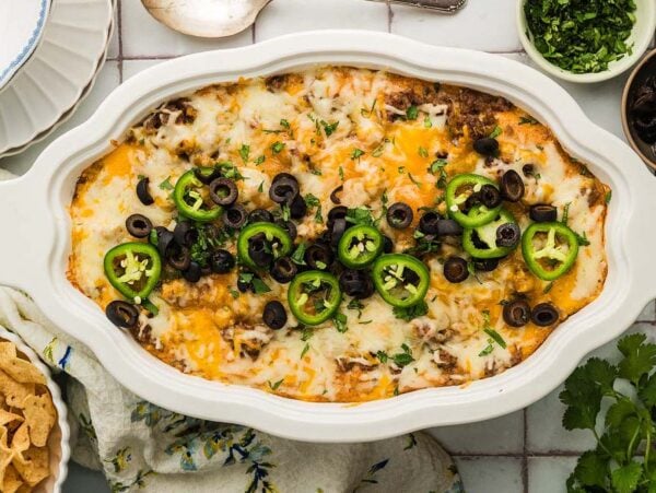 Texas Trash Dip baked casserole topped with melted cheese, jalapeño slices, and black olives, surrounded by chips and herbs.