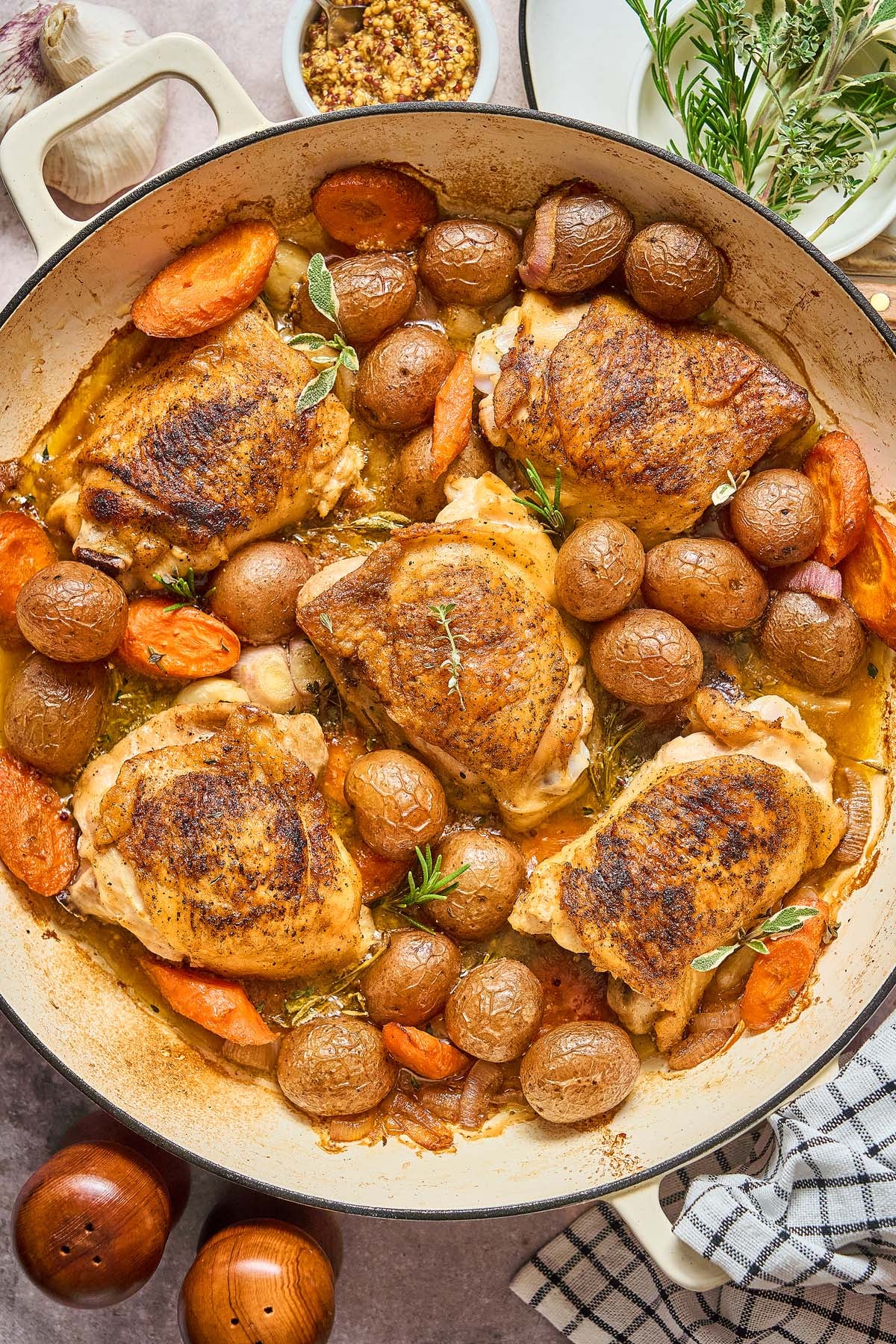 Beer Braised Chicken Thighs with baby potatoes and carrots roasted in a large pan, garnished with fresh herbs.