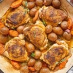 Beer Braised Chicken Thighs baked with baby potatoes and carrots in a large skillet, garnished with fresh herbs.