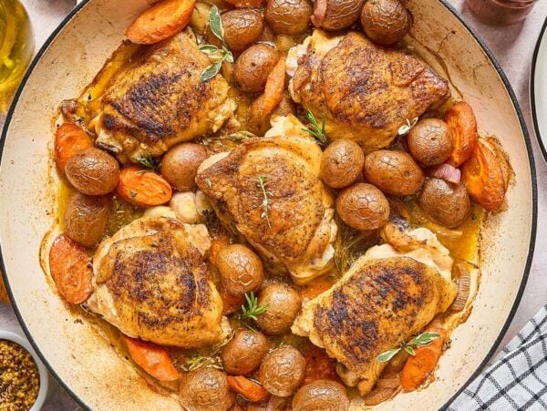 Beer Braised Chicken Thighs baked with baby potatoes and carrots in a large skillet, garnished with fresh herbs.