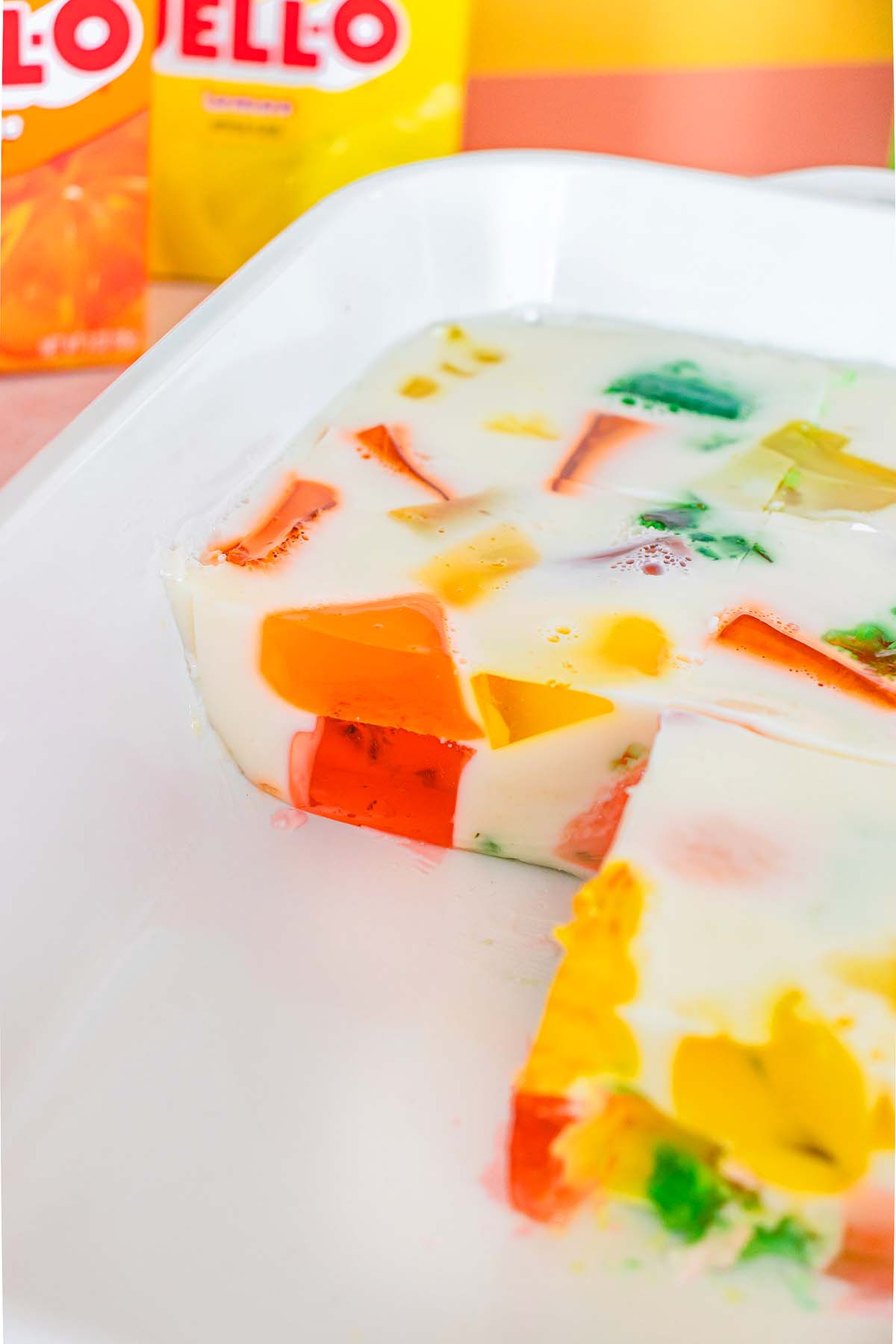 A dish of colorful Broken Glass Jello cubes set in a creamy white mixture, with a slice removed.