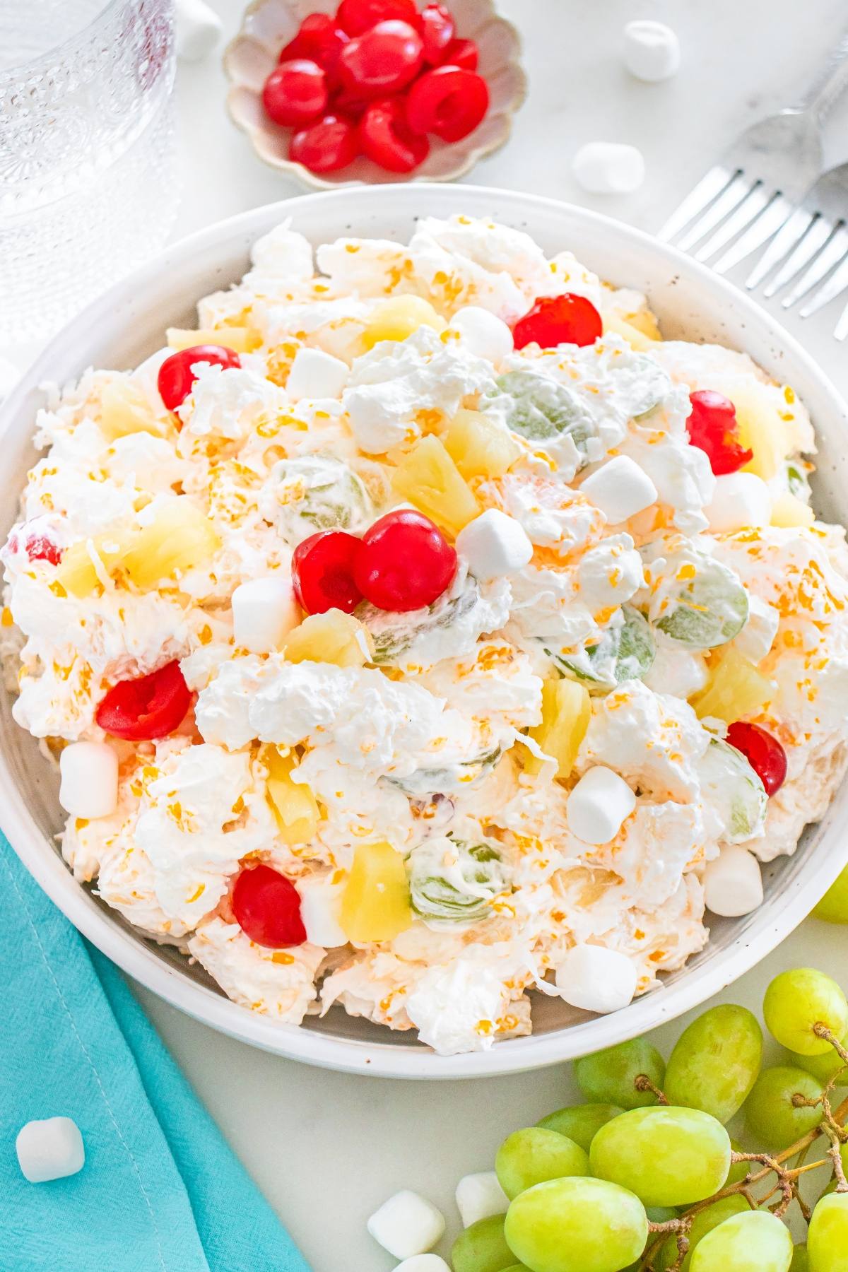 A bowl of fluffy ambrosia salad topped with cherries, pineapple, grapes, and mini marshmallows.