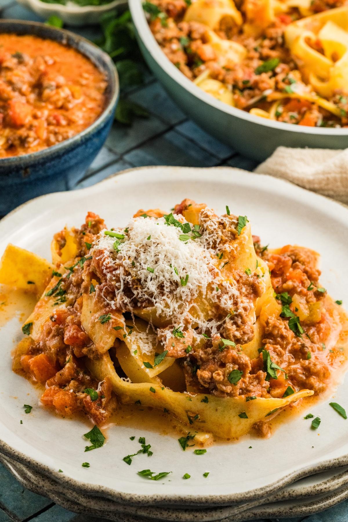 A plate of tagliatelle pasta topped with meat authentic bolognese sauce and grated cheese, with more pasta and sauce in the background.