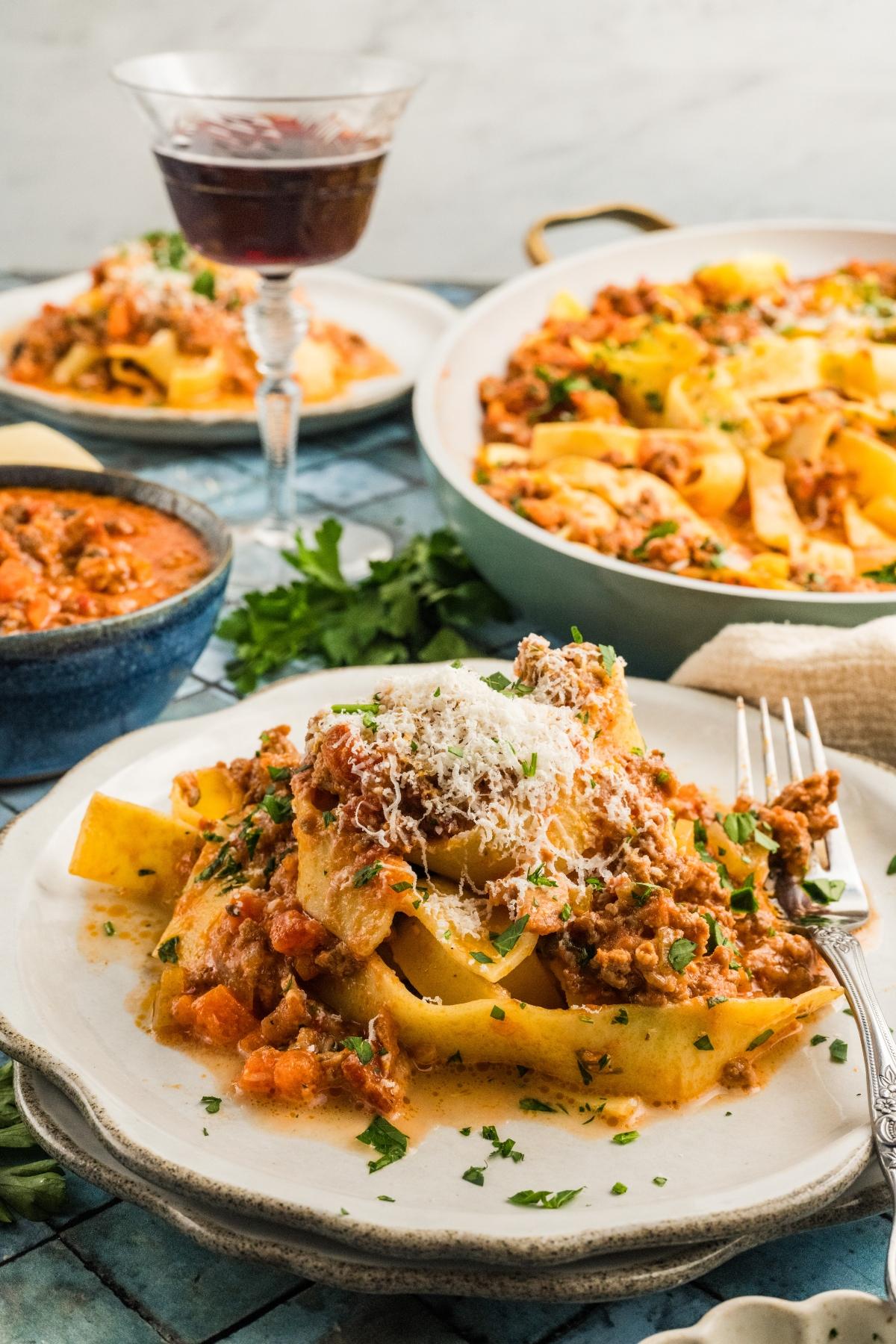 A plate of pasta with meat authentic bolognese sauce and grated cheese, surrounded by more pasta dishes and a glass of red wine.