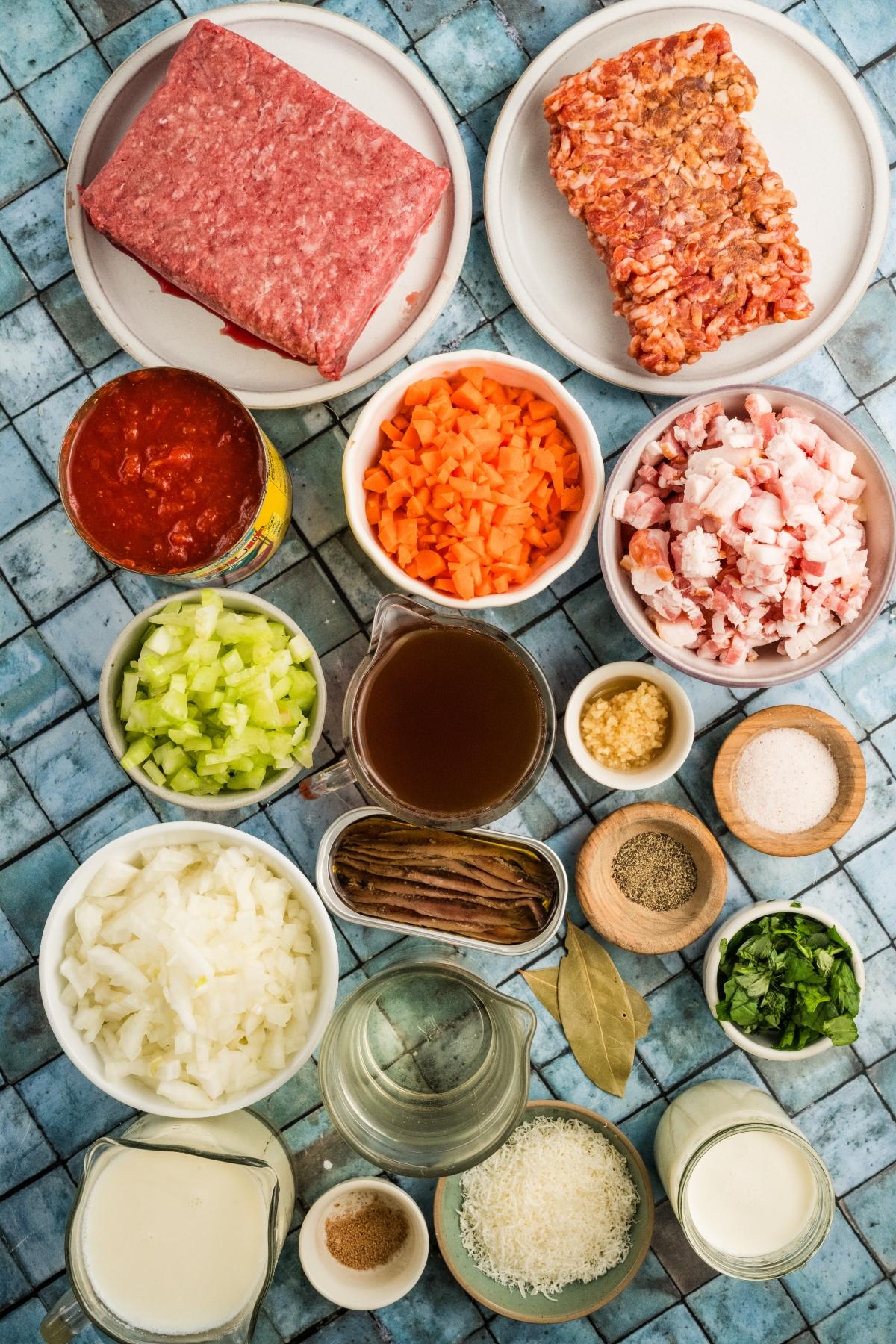 Ingredients for a meat sauce, including ground meat, chopped vegetables, herbs, broth, dairy, and seasonings.