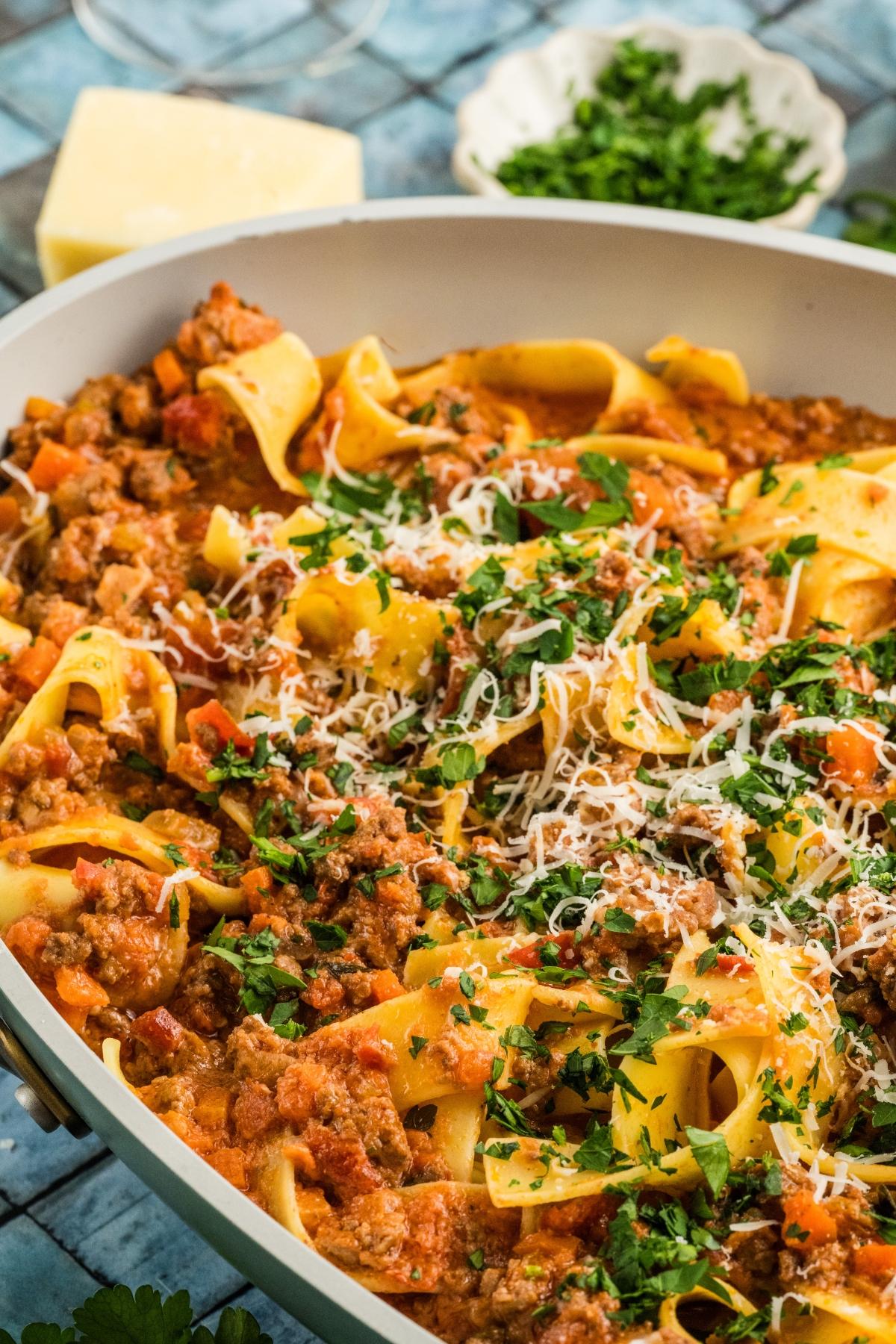 Wide skillet of pappardelle pasta with meat authentic bolognese sauce, topped with chopped parsley and grated cheese.