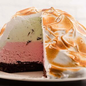 A classic Baked Alaska dessert with a slice cut out, revealing layers of ice cream and cake beneath perfectly toasted meringue.