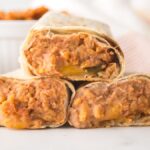 Three bean and cheese burritos stacked on a white surface with a garnish of fresh parsley nearby, highlighting the classic appeal of bean and cheese burritos.
