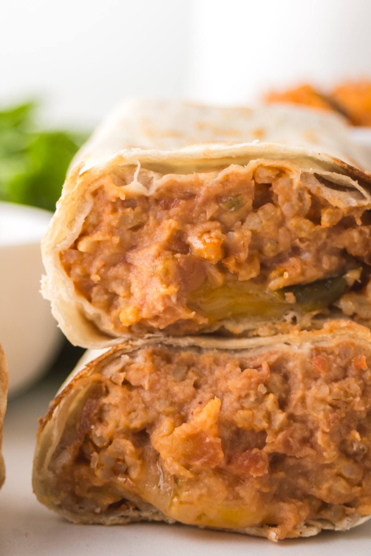 Close-up of two stacked bean and cheese burritos with a creamy filling visible inside the cut tortillas.