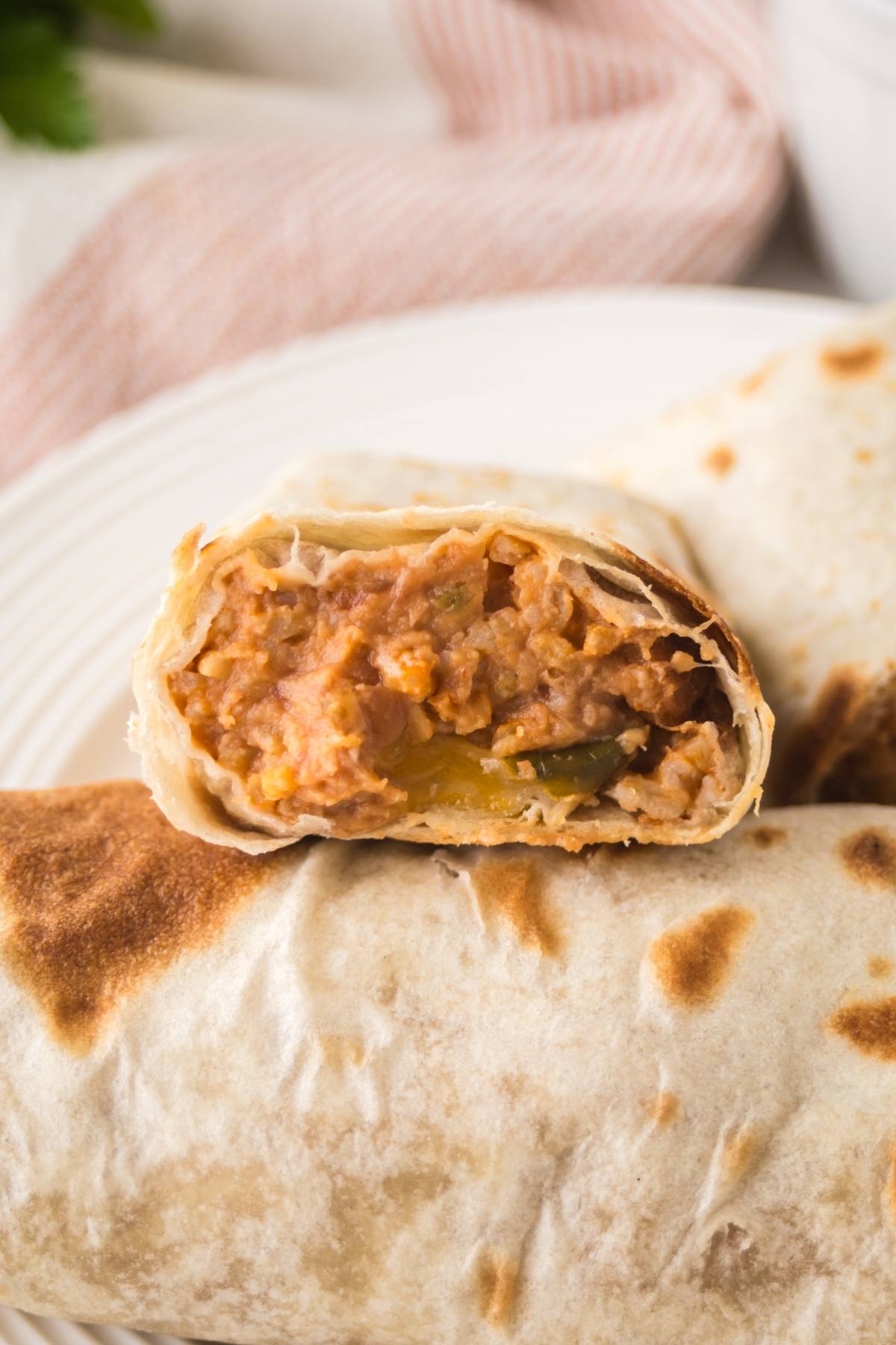 A close-up of a bean and cheese burrito cut in half, showing a filling of beans, cheese, and vegetables on a plate.