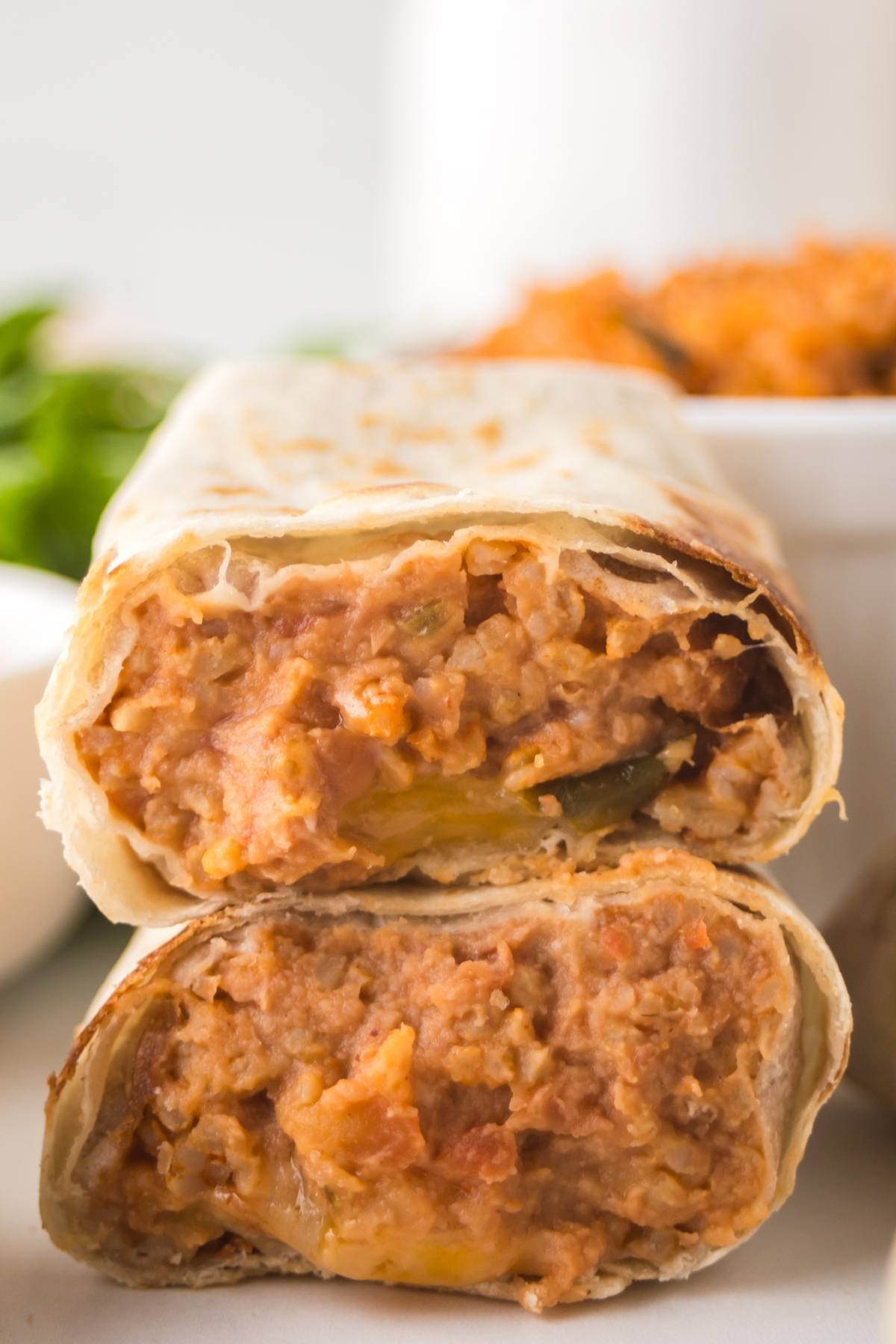 Close-up of two stacked bean and cheese burritos cut in half, showing a creamy, cheesy bean and tomato filling.