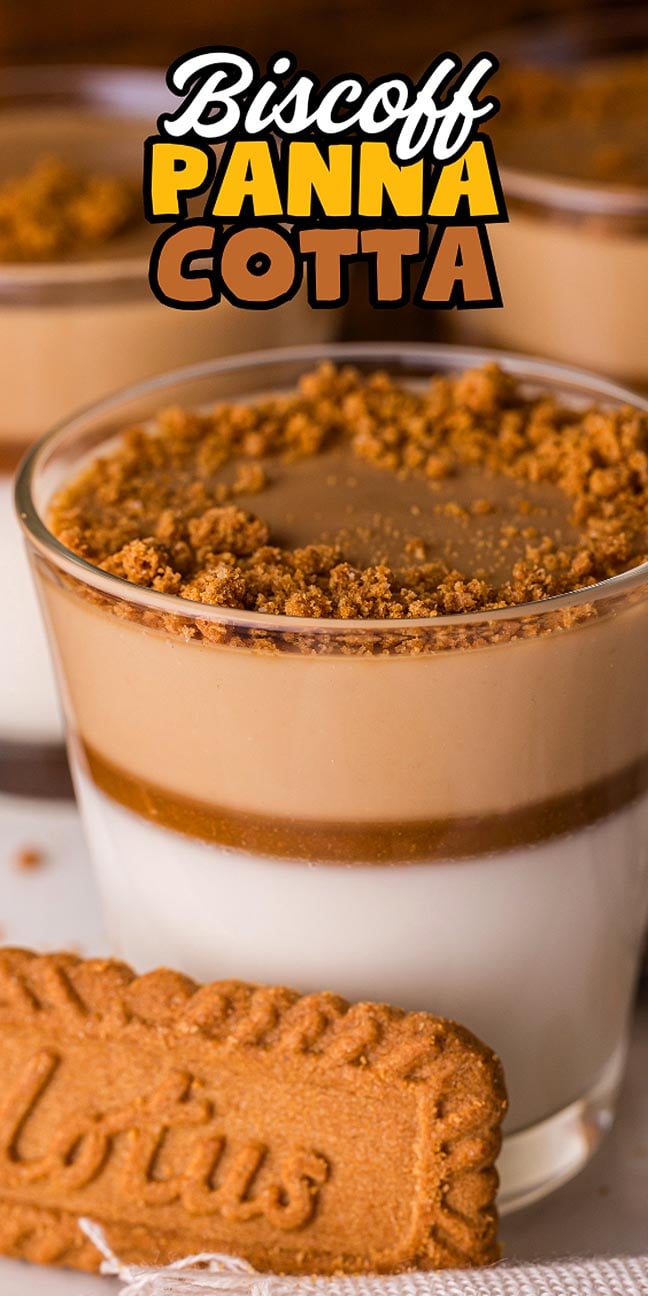 A glass of creamy Biscoff Panna Cotta topped with crushed Biscoff cookies and finished with a whole Lotus biscuit in front.