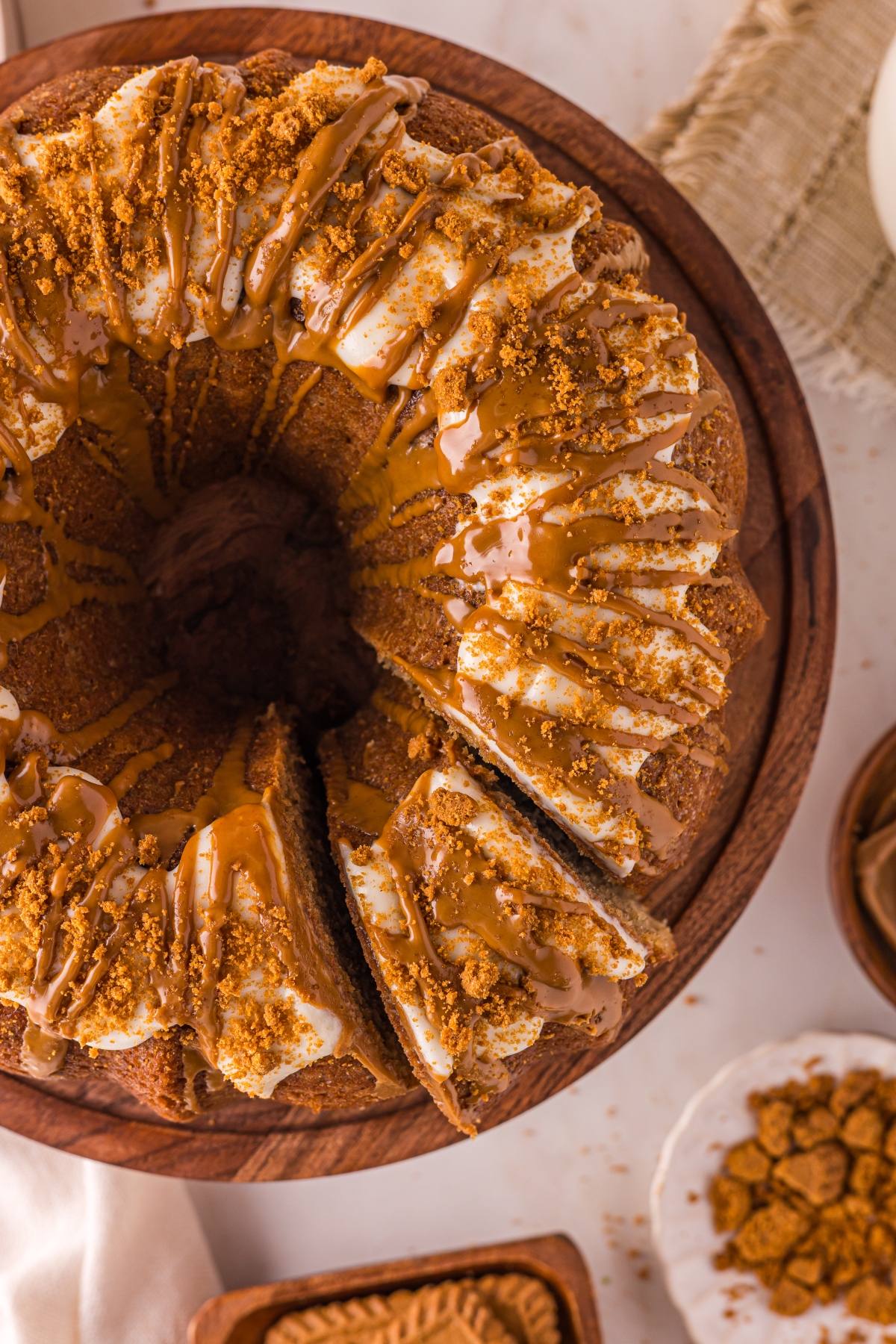 A biscoff cake with icing and cookie crumbs, sliced and displayed on a wooden cake stand.