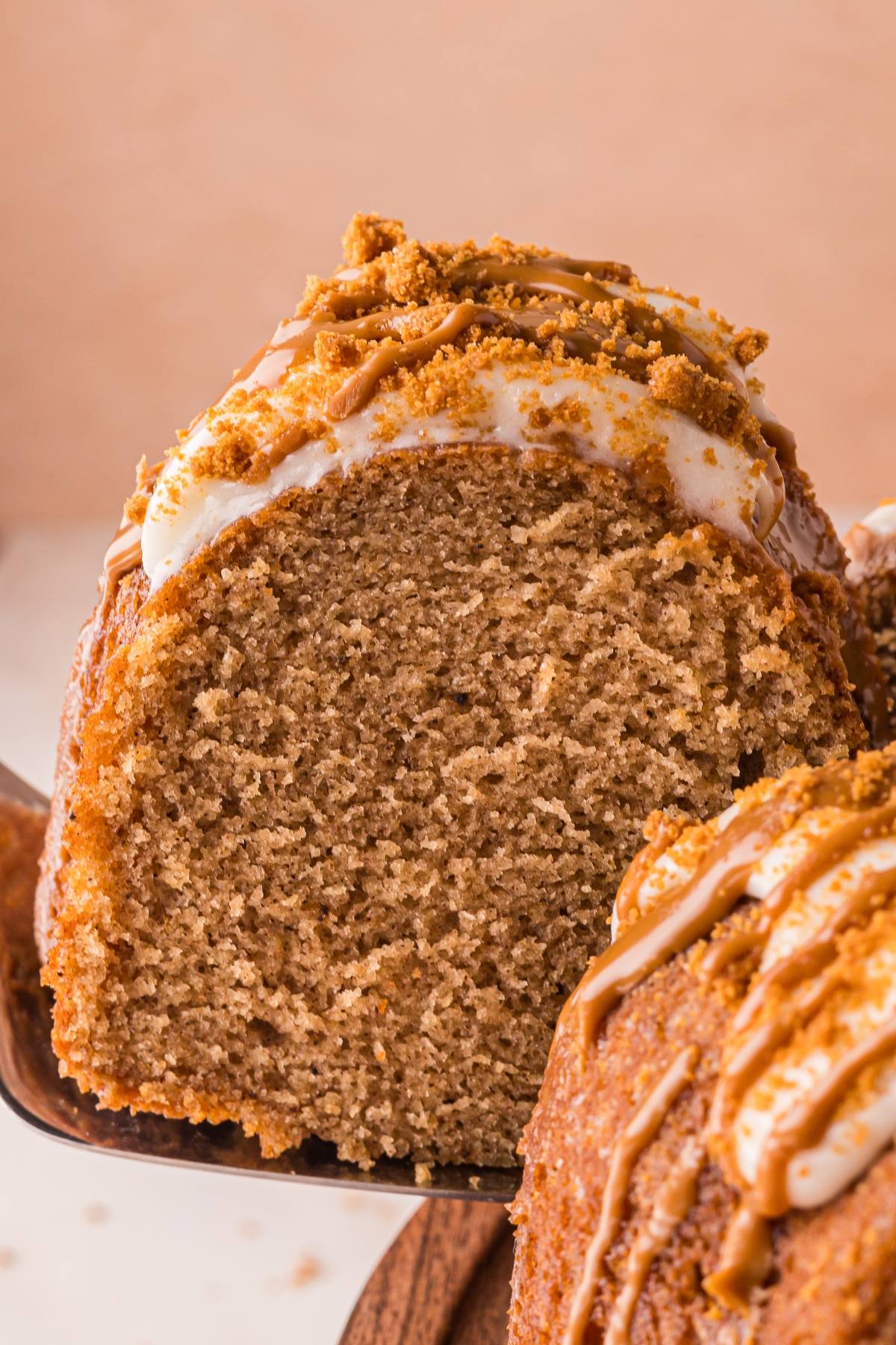 A close-up of a slice of spiced biscoff cake with icing and cookie crumbles on top.