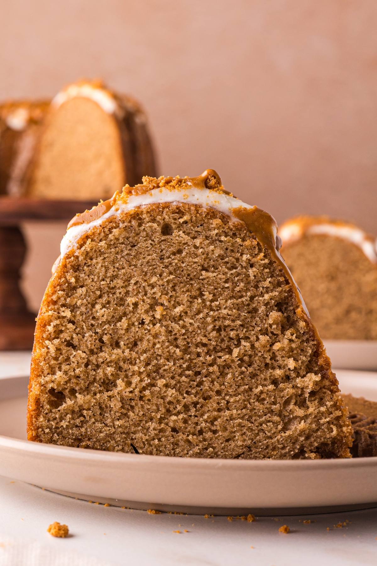 A close-up of a slice of biscoff cake with icing on a plate; more cake is visible in the background.