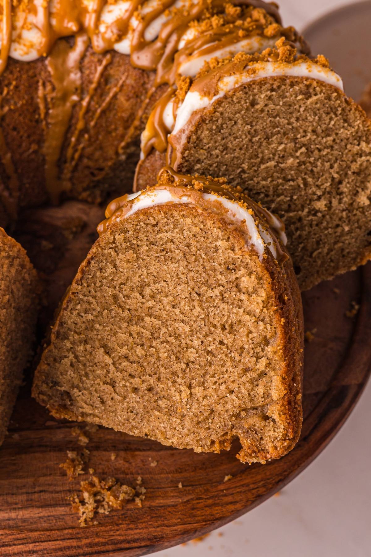 A close-up of a sliced biscoff cake with icing and caramel drizzle on a wooden plate.