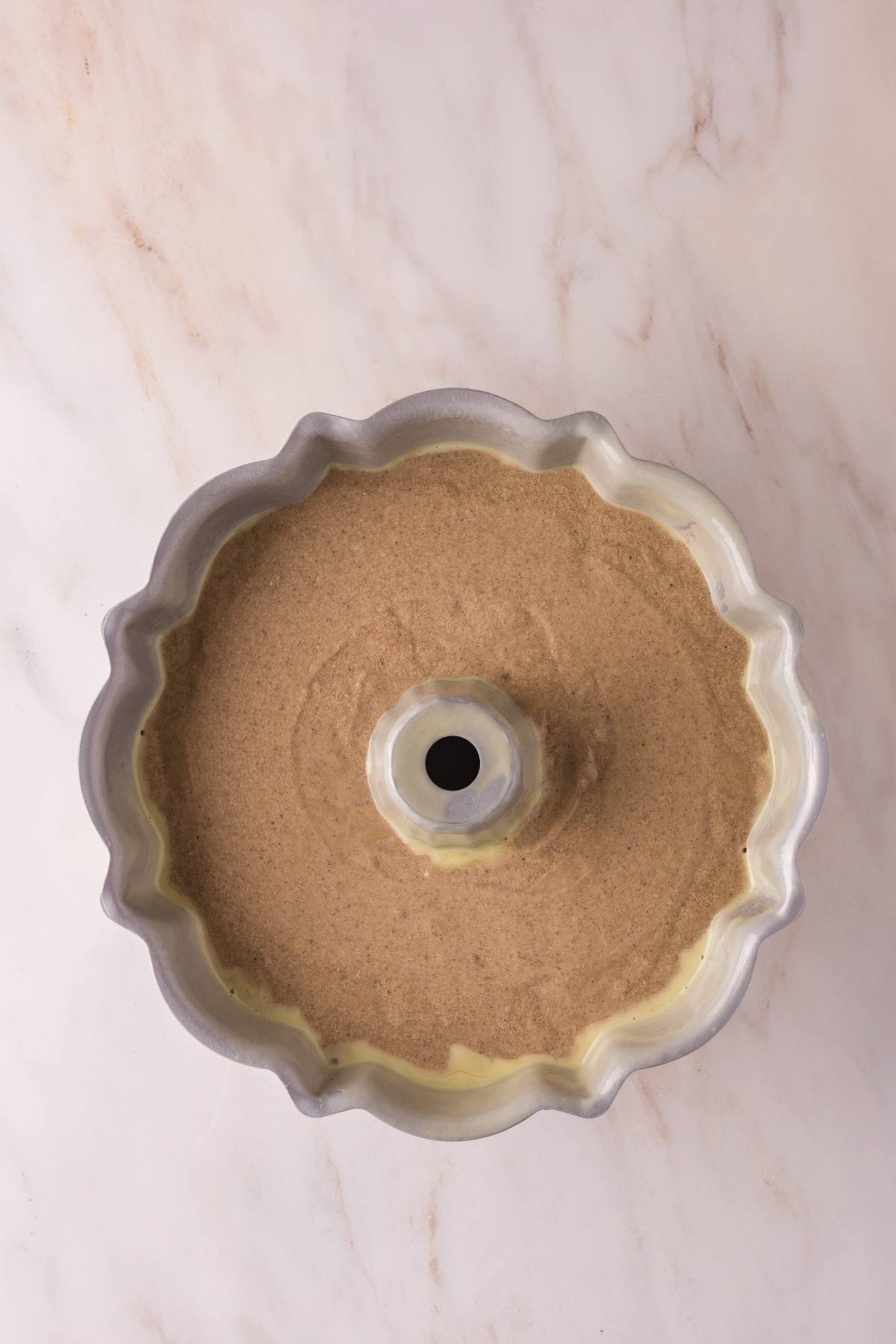 Bundt cake pan filled with brown batter, ready to be baked, on a light marble surface.