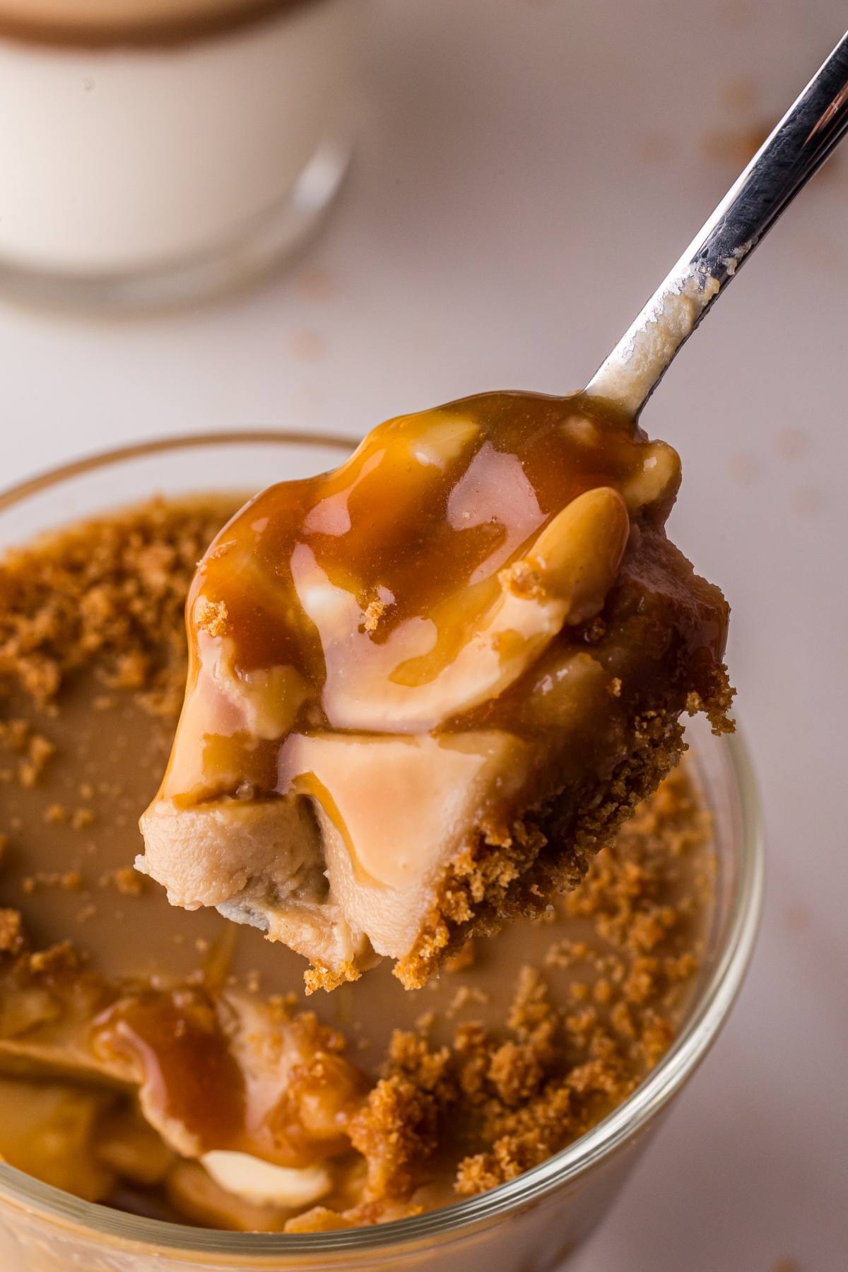 A spoonful of creamy biscoff panna cotta  dessert with caramel sauce and crumbled cookie topping above a glass cup.