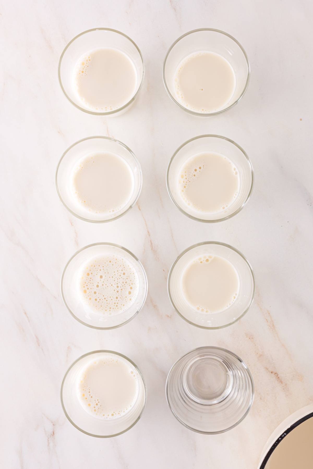 Seven glasses, six filled with milk and one empty, arranged in two vertical columns on a white surface.