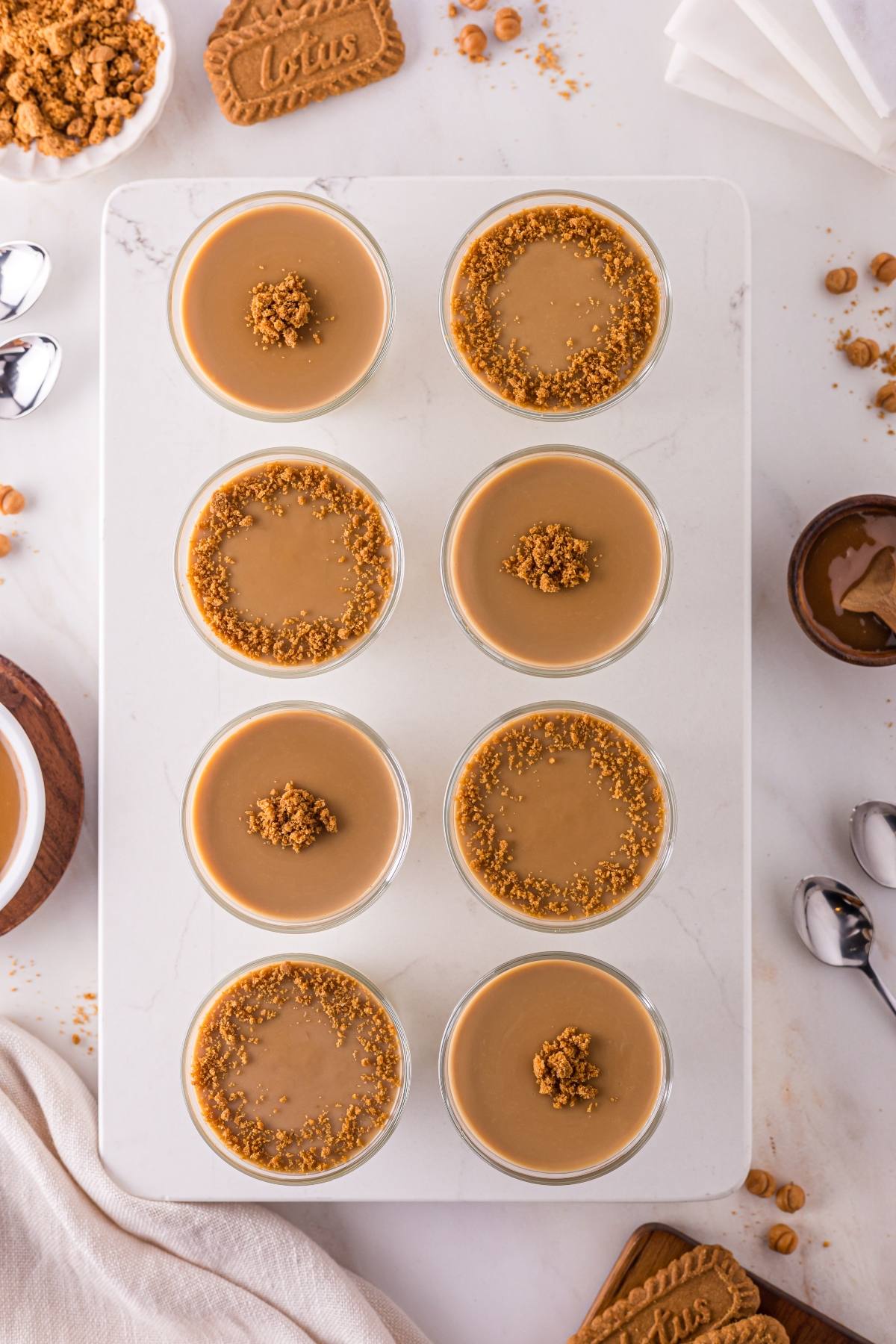 Eight glass cups of creamy dessert topped with cookie crumbs, arranged neatly on a white tray.
