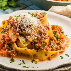 Pasta topped with authentic Bolognese sauce and grated cheese, served on a white plate with a parsley garnish.